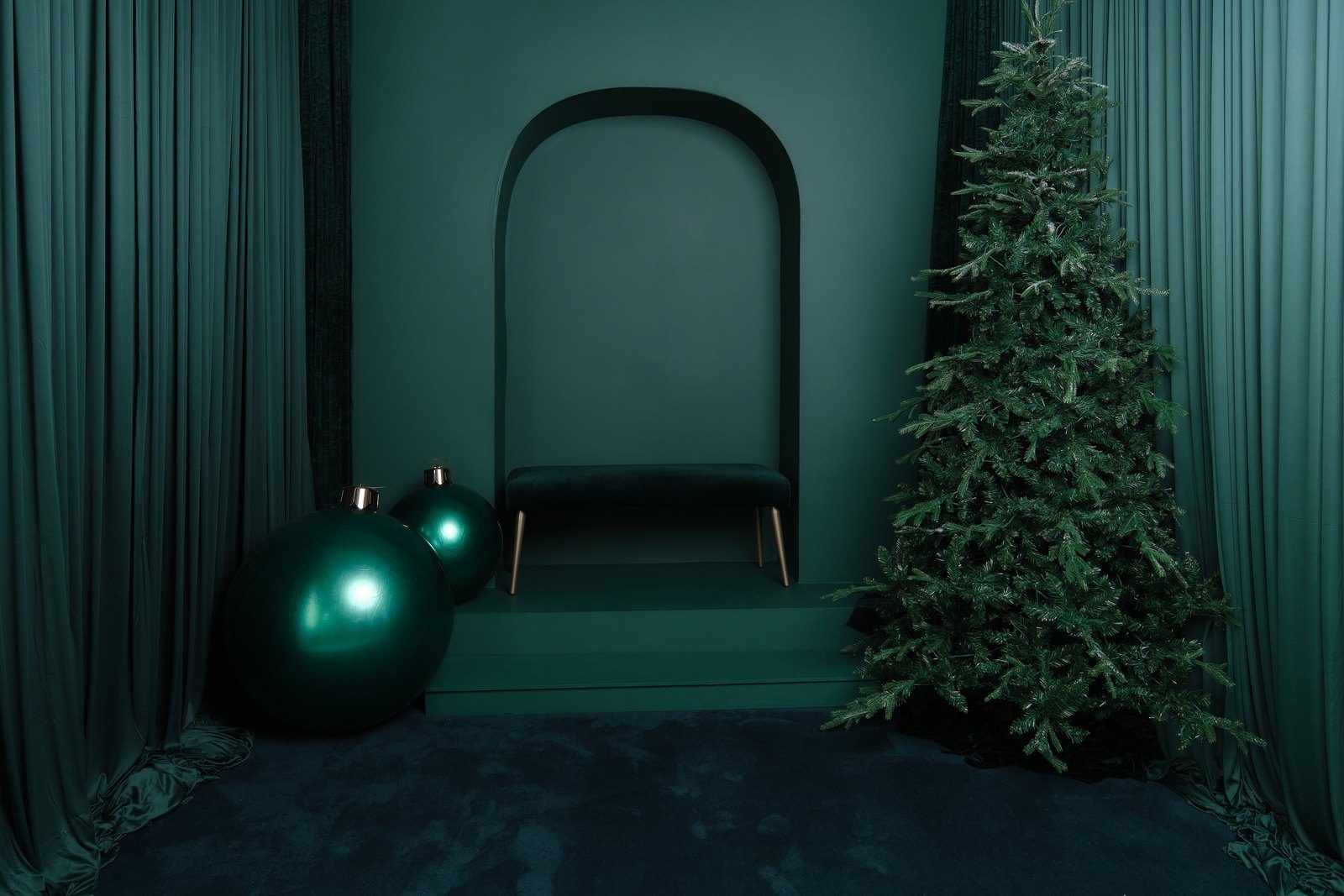 A deep emerald green studio set with an arched alcove, velvet bench and dark tree