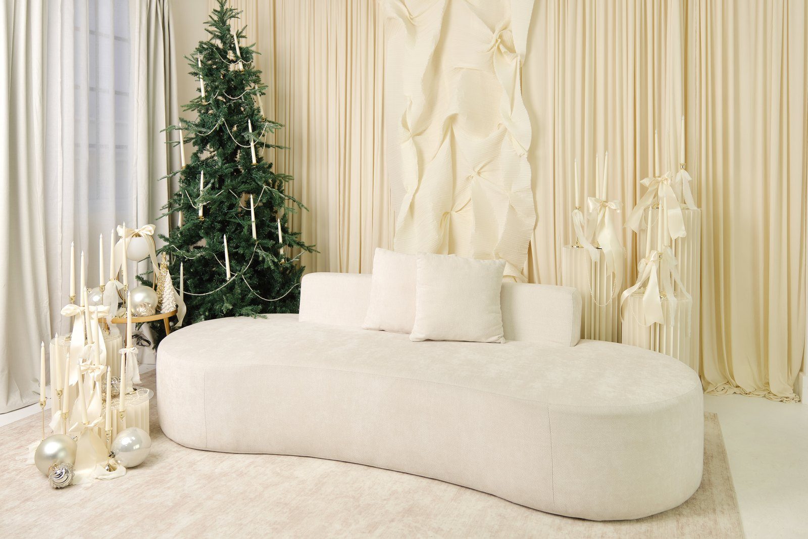 A studio set dressed in cream and ivory with a curved sofa and a candle-lit tree