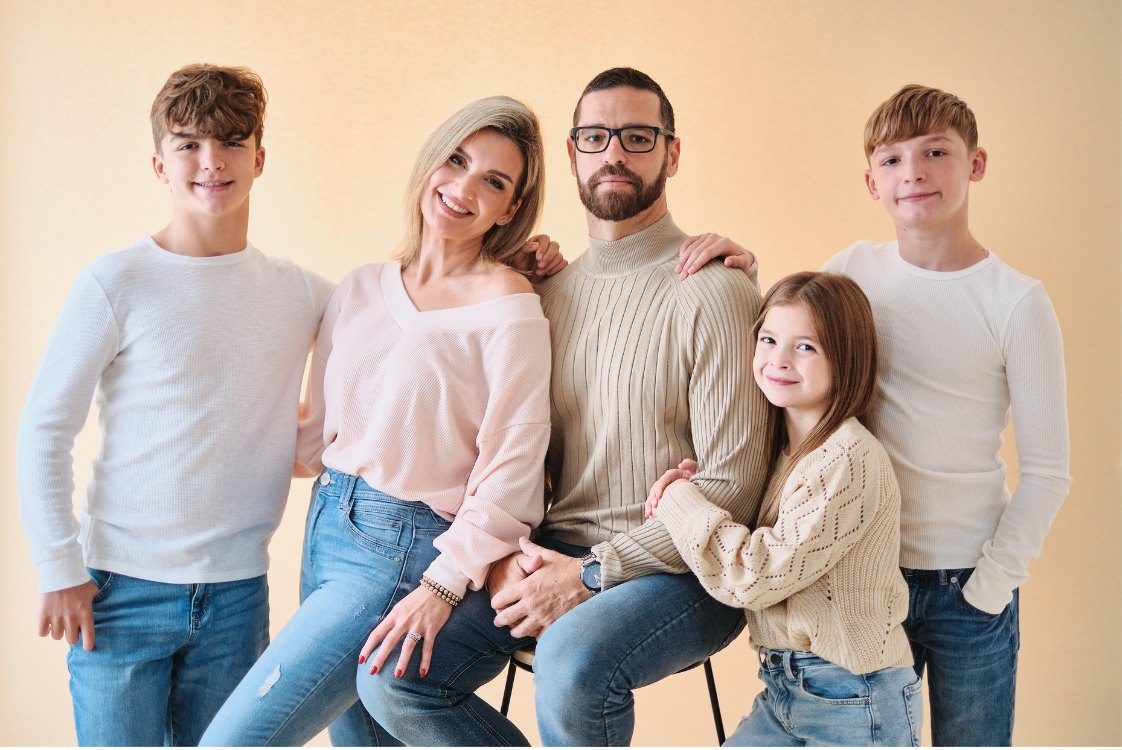A family of six in cream knits and denim against a warm sand backdrop