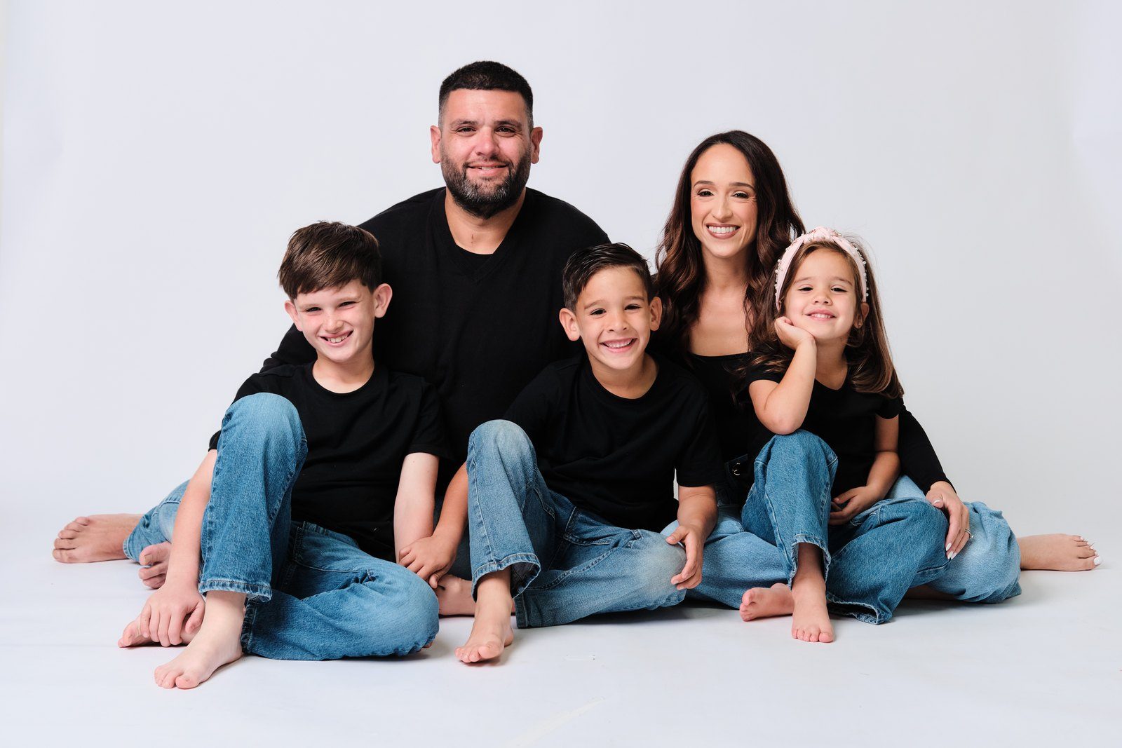 A family of five in black tops and jeans seated together against a pure white background