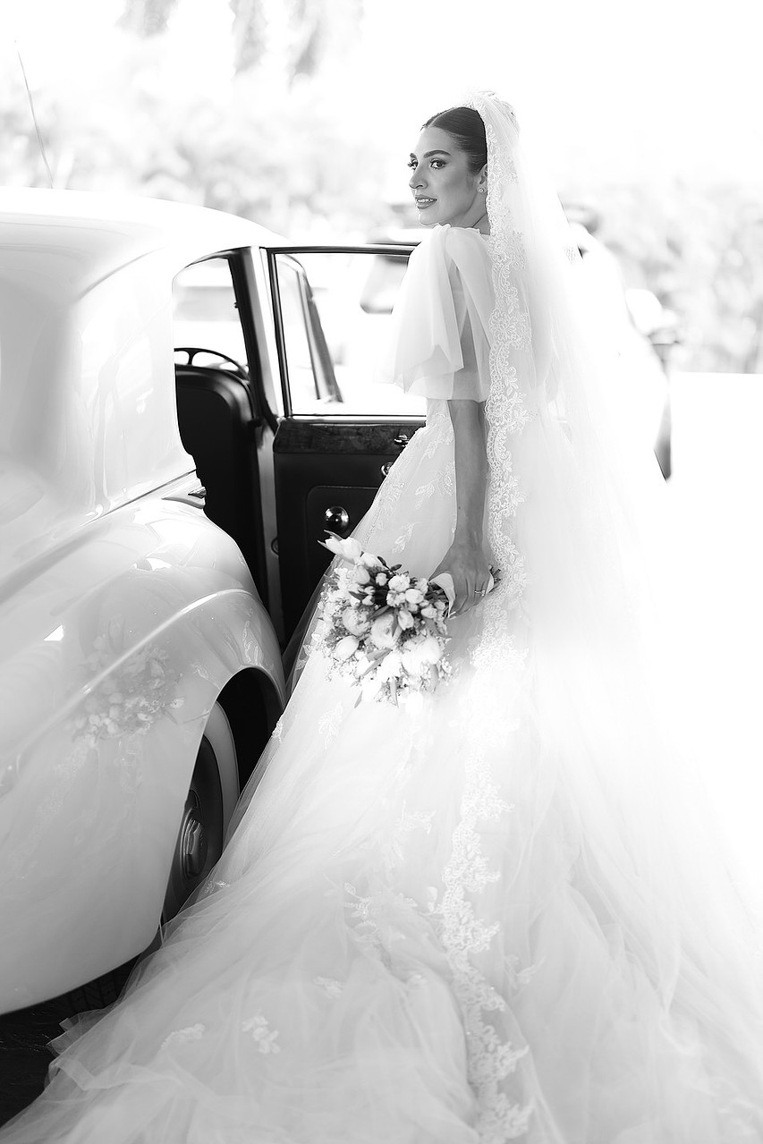 An editorial black-and-white portrait of a bride with a vintage car